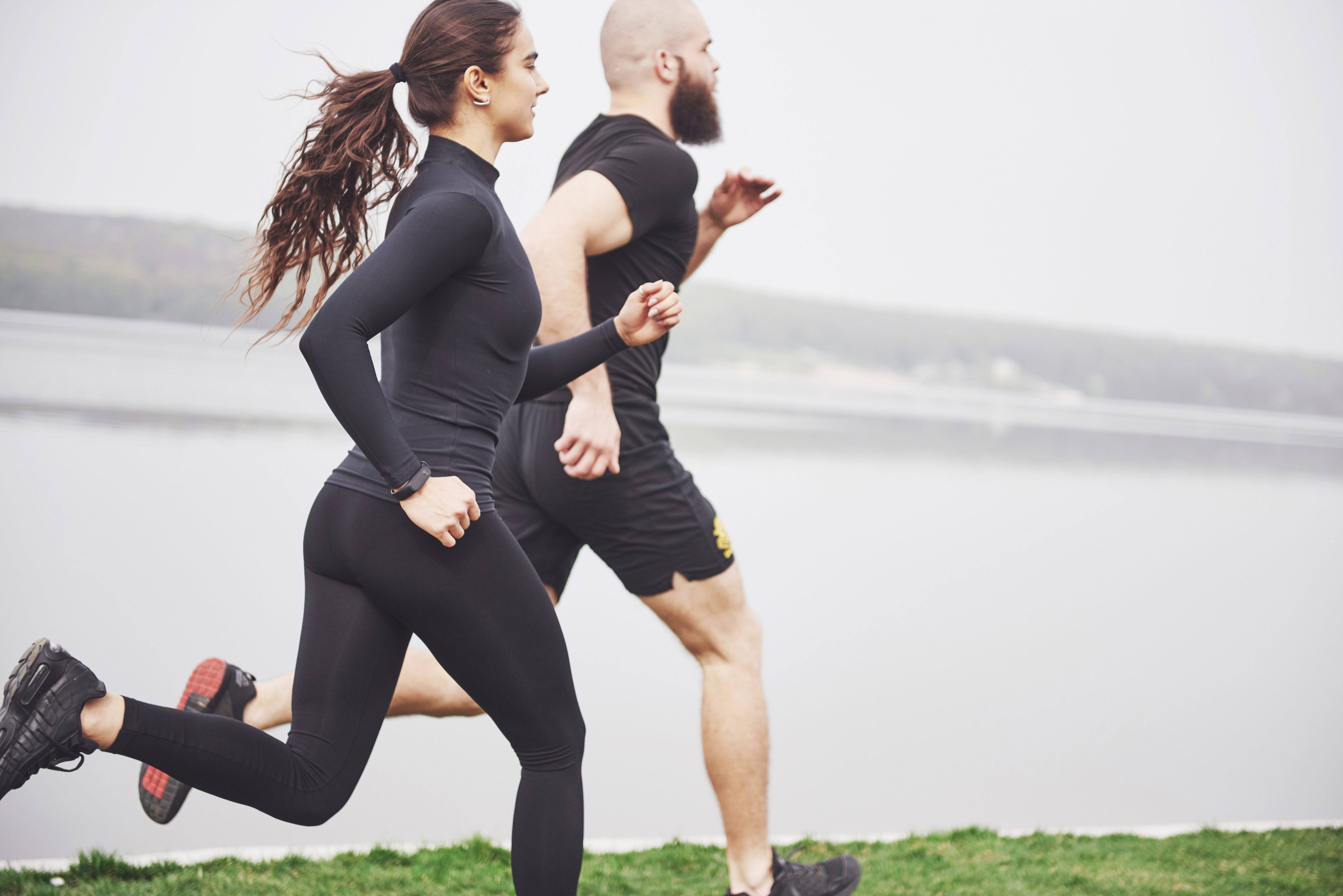 Couple jogging and running outdoors in park near the water. Young bearded man and woman exercising together in morning.